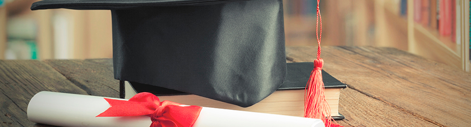 Un libro, un diploma y un birrete sobre una mesa en una biblioteca
