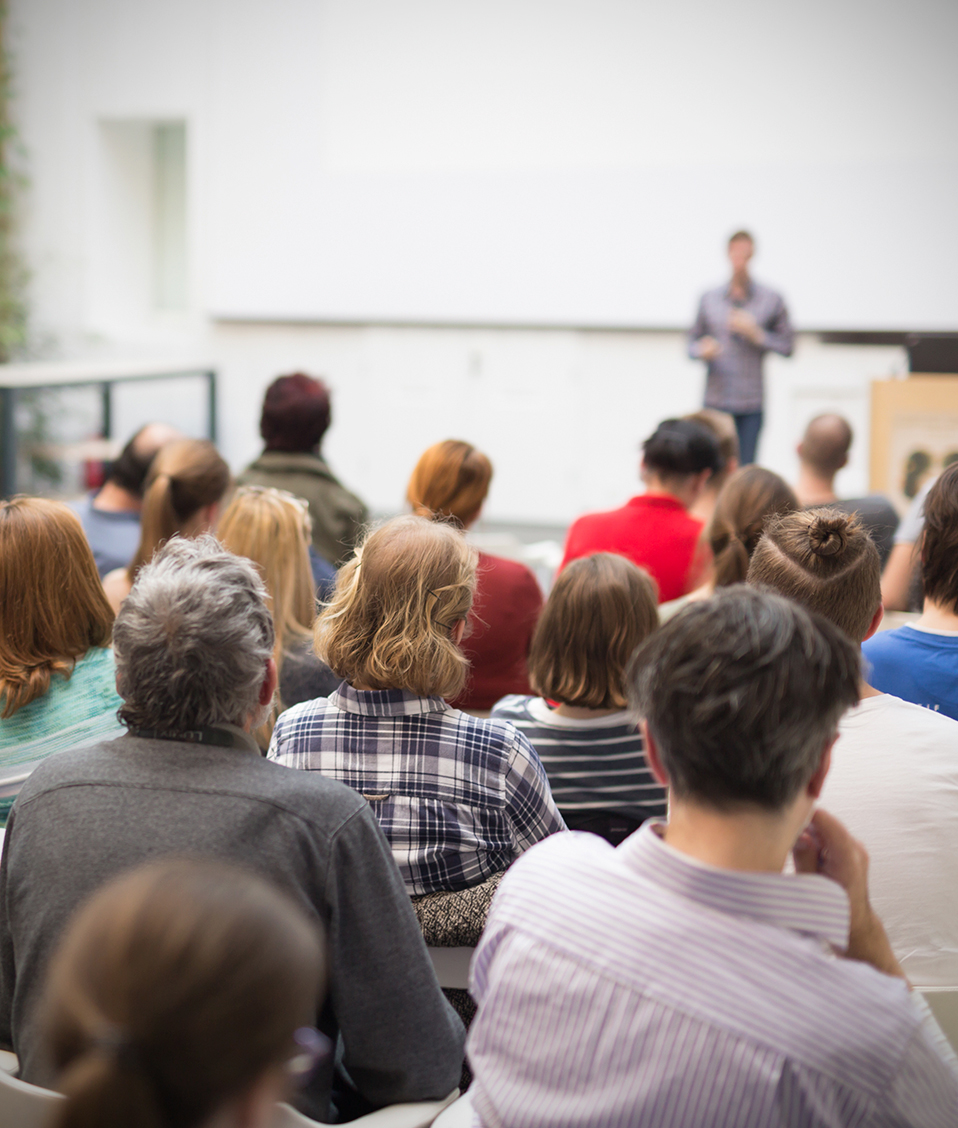 Una conferencia es impartida al aire libre, el público lo componen personas de diferentes edades