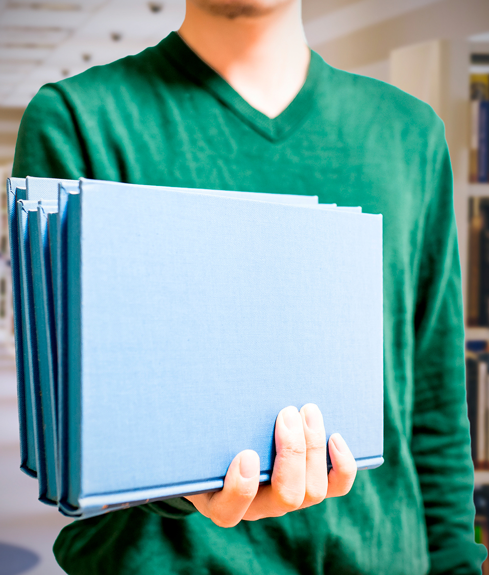 Primer plano de un estudiante sujetando diversos libros de tapa azul en una de las bibliotecas de la Universidad de Granada